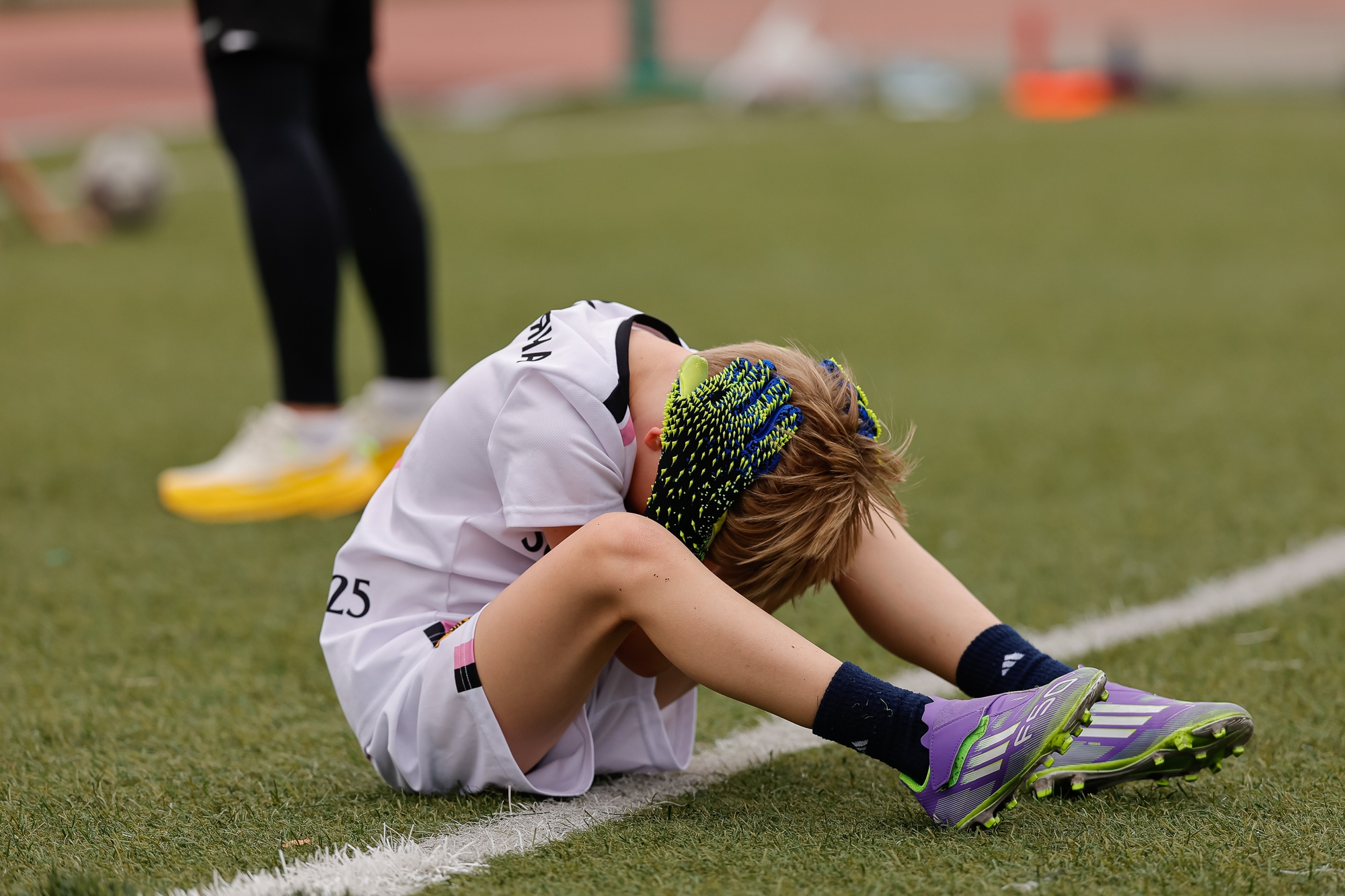 Ребенок футболист сидит на газоне футбольного поля и держится за голову