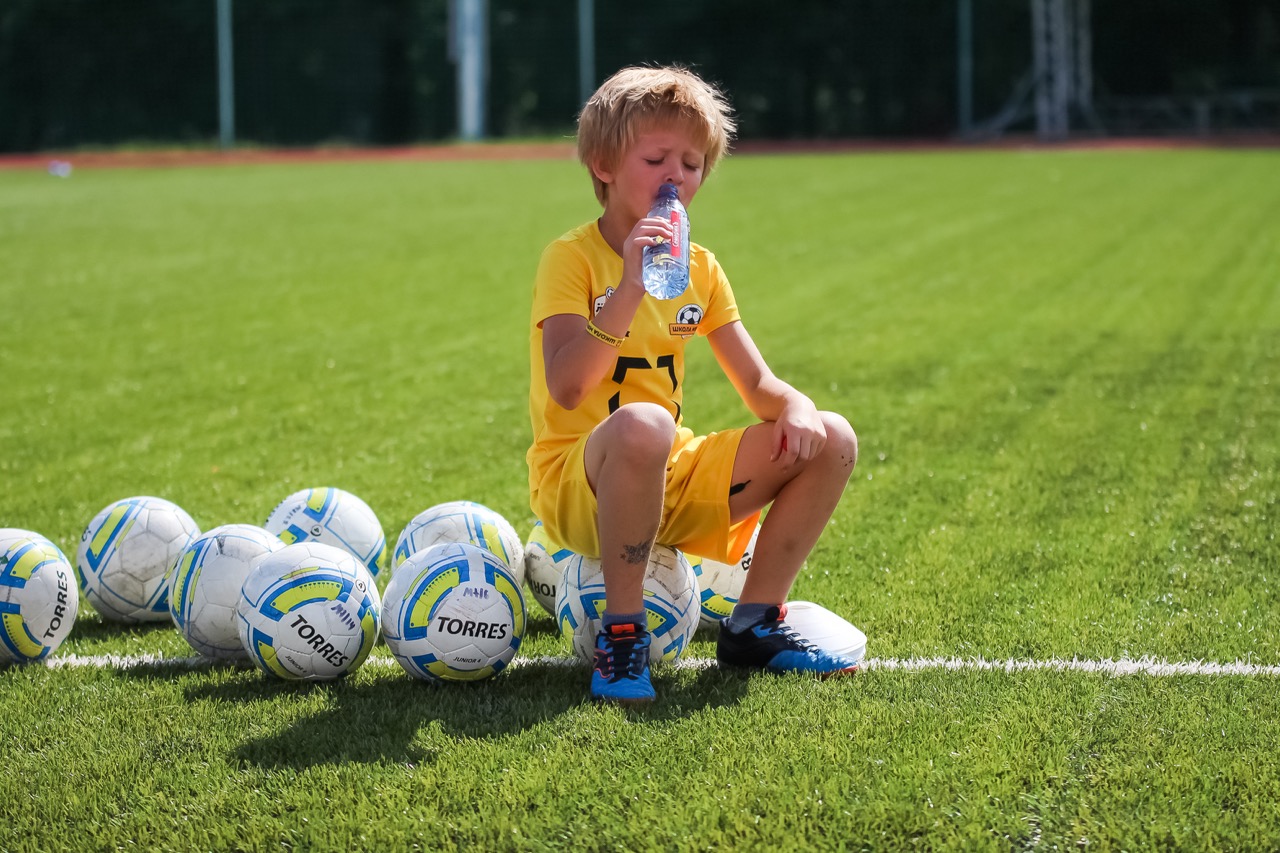 Ребенок футболист пьет воду и отдыхает