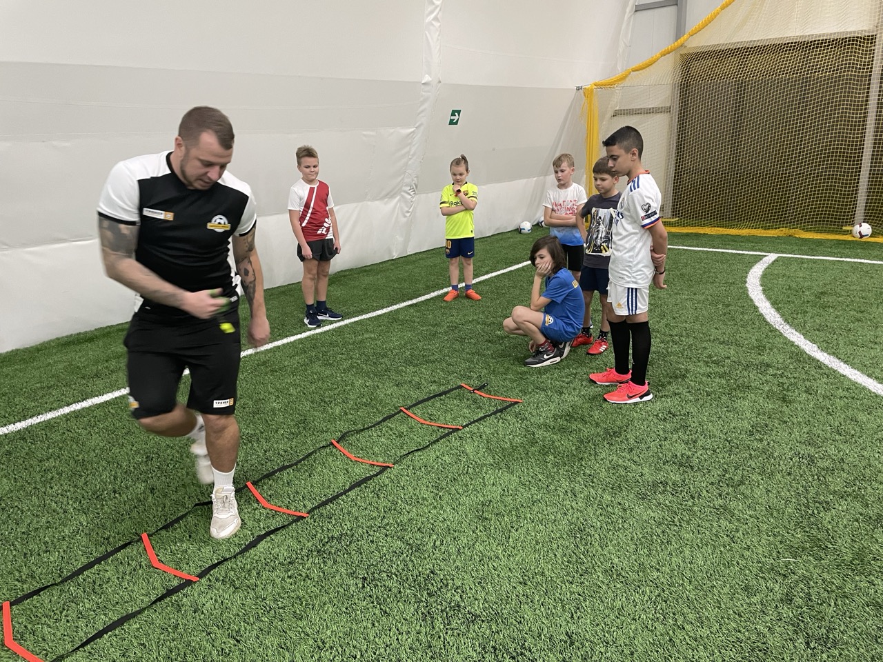 Футбольный тренер показывает как выполнять футбольное упражнение с лесенкой