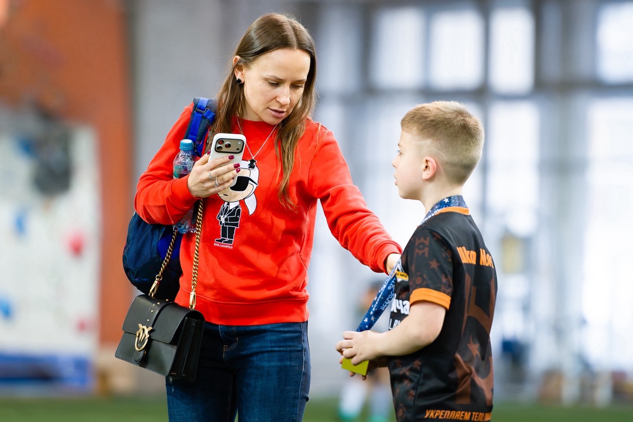 Мама провожает ребенка футболиста в спортивный лагерь Школы мяча
