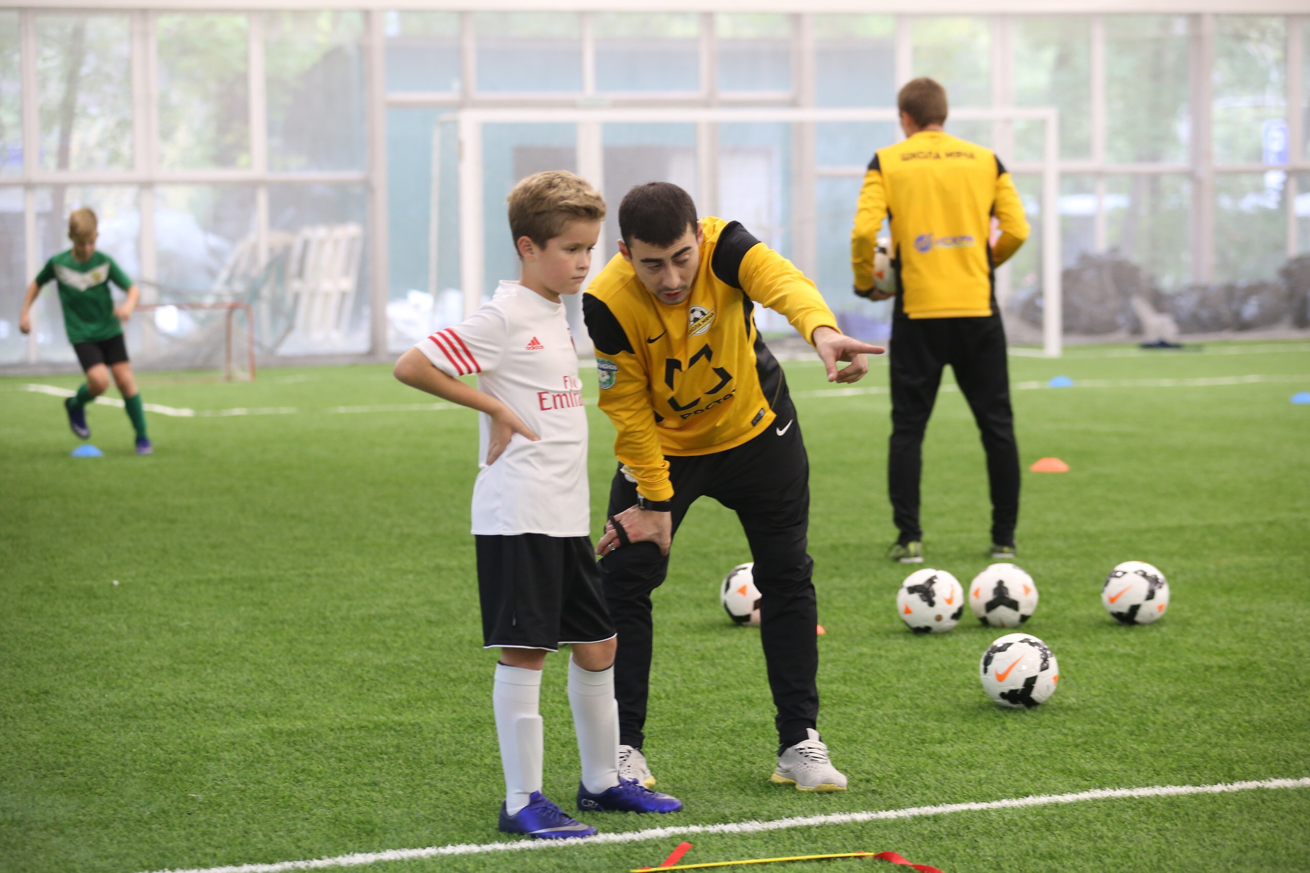 Тренер Школы мяча дает совет ребенку футболисту на открытом уроке