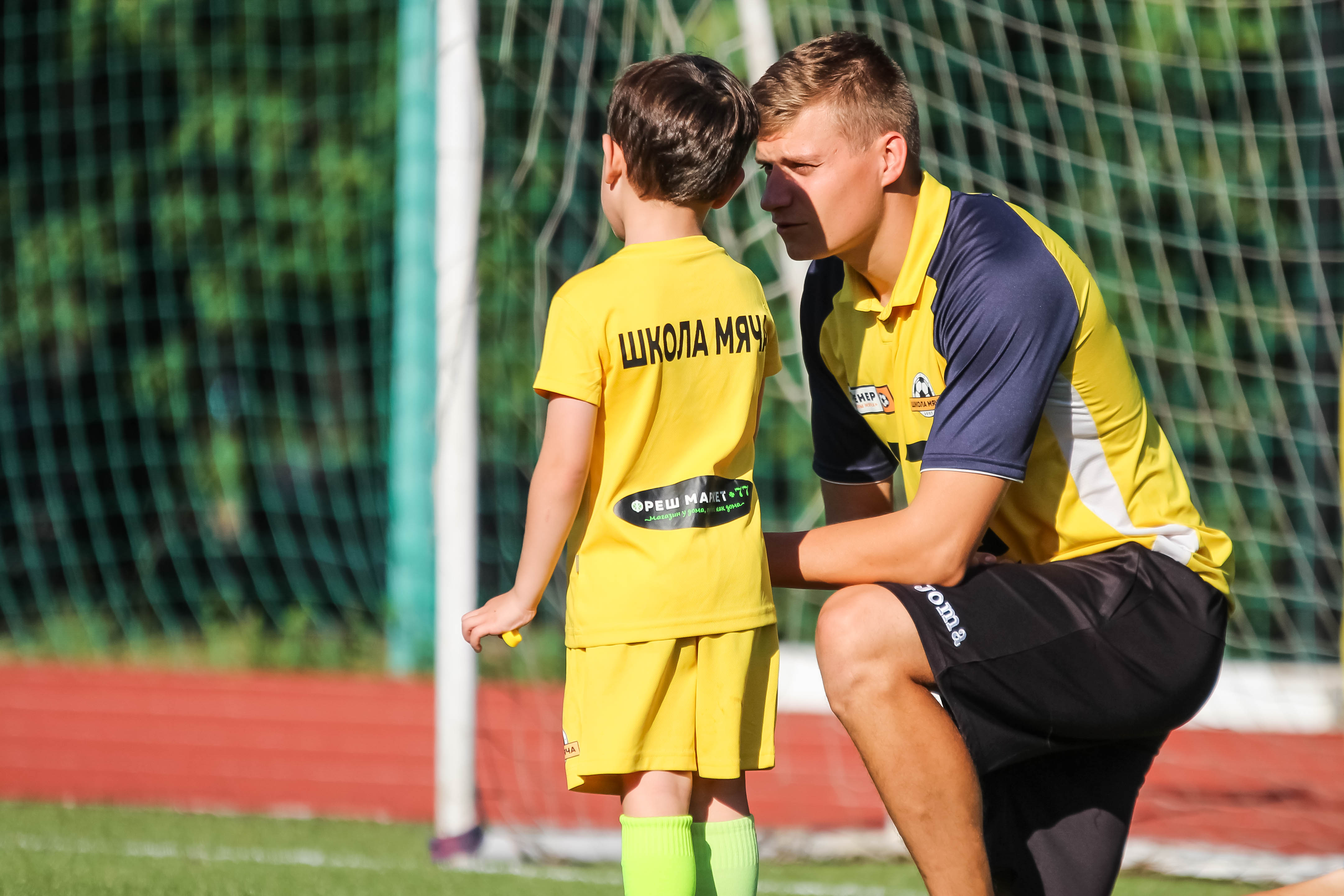 Футбольный тренер Школы мяча общается с ребенком футболистом на поле